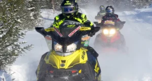 a line of snowmobilers traveling down a snowy rail during the day