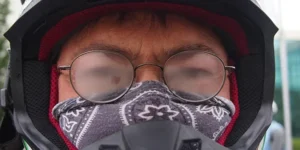 man in a snowmobile helmet and a bandana over his nose and mouth squints to try to see through his fogged up glasses