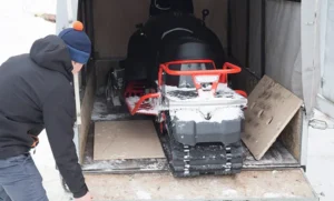 a man dressed in winter gear packs his snowmobile in his trailer