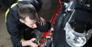 a mechanic squats next to a snowmobile with a light in his hand looking at the suspension