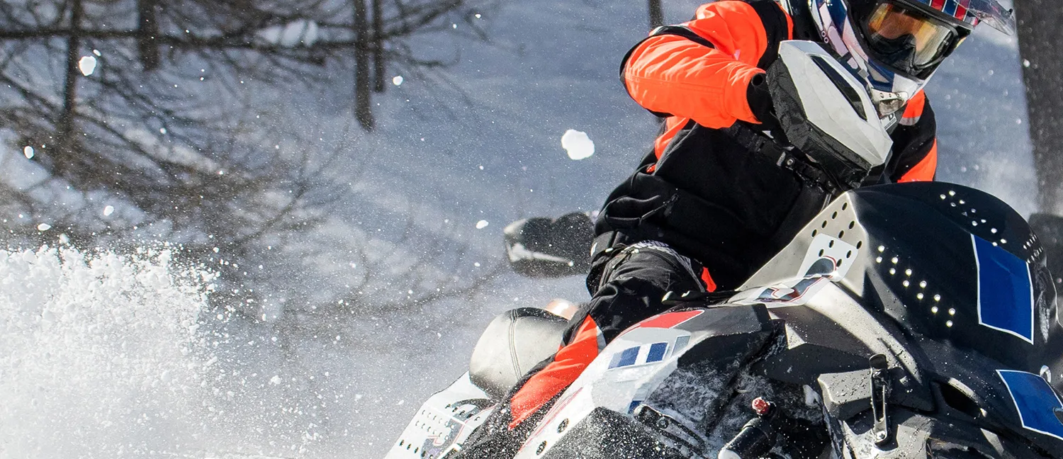 a rider in winter gear rips away on his snowmobile spraying snow behind him