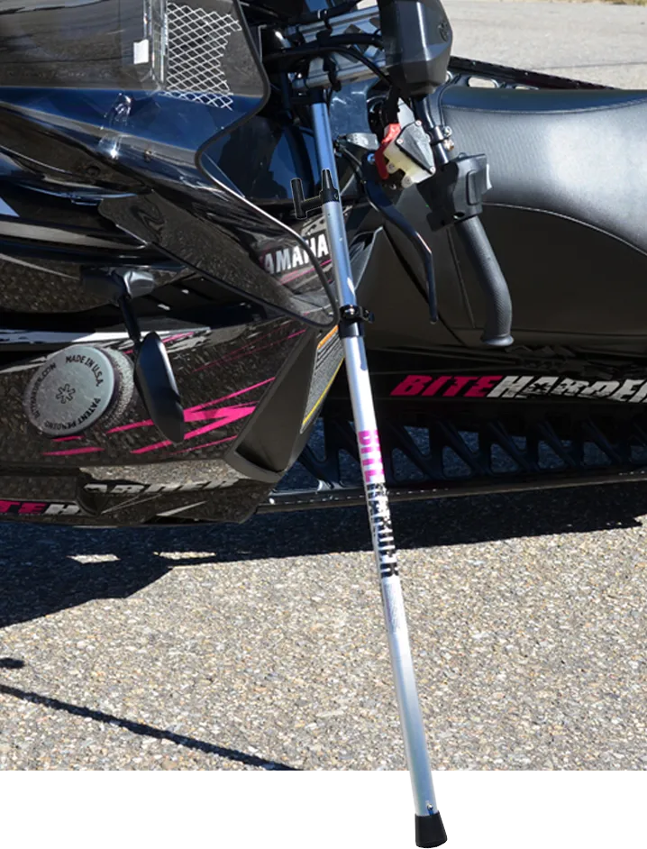 a snowmobile in a parking lot, on it's side supported by biteharders side support pole