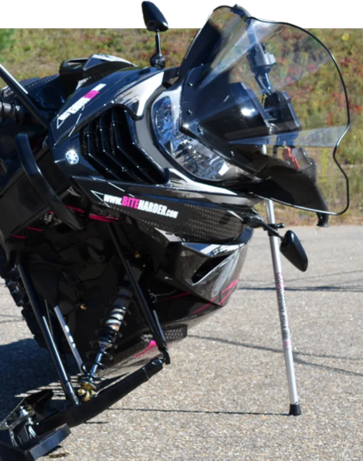 a snowmobile in a parking lot, on it's side supported by biteharders side support pole