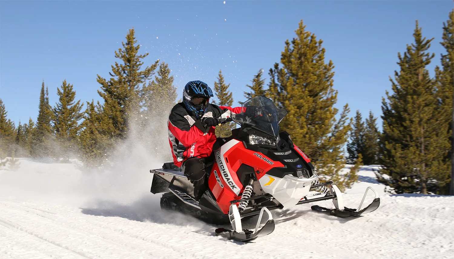 snowmobiler rips past pine trees in red and black gear that matches his snowmobile